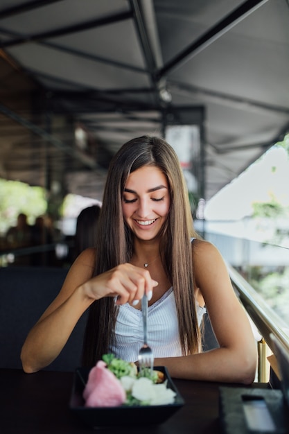 Mujer joven comiendo comida saludable sentado en el hermoso interior