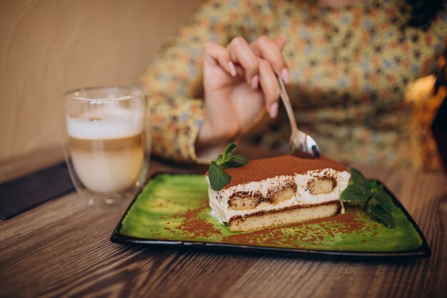 Mujer joven comiendo delicioso tiramisú en un café