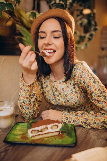 Mujer joven comiendo delicioso tiramisú en un café