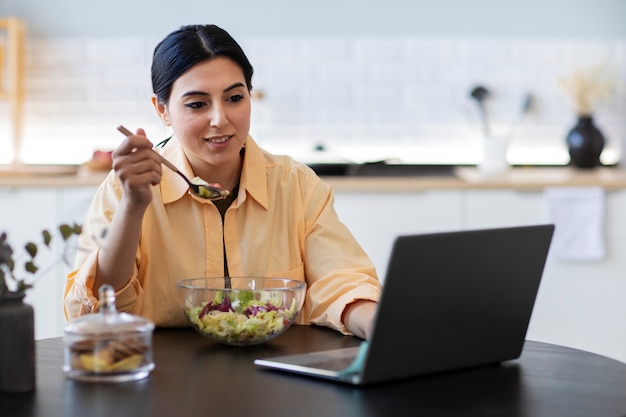 Mujer joven comiendo ensalada y viendo video