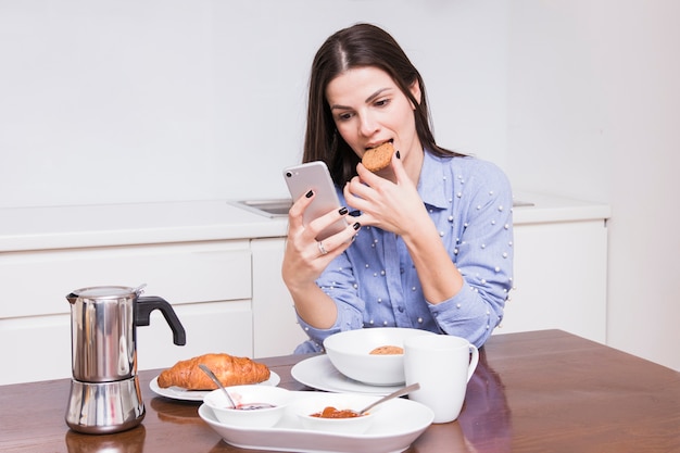 Mujer joven comiendo galletas desayunando en la cocina