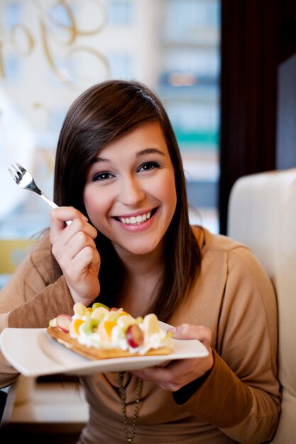 Mujer joven comiendo gofres con crema batida y frutas