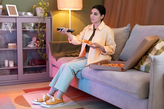 Mujer joven comiendo pizza y viendo la televisión