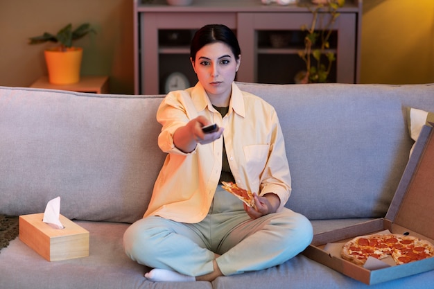 Mujer joven comiendo pizza y viendo la televisión