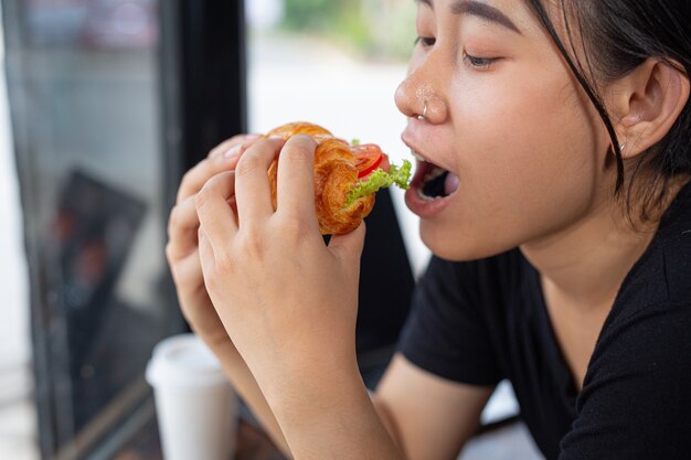 Mujer joven comiendo sándwiches de croissant en la sala de oficina