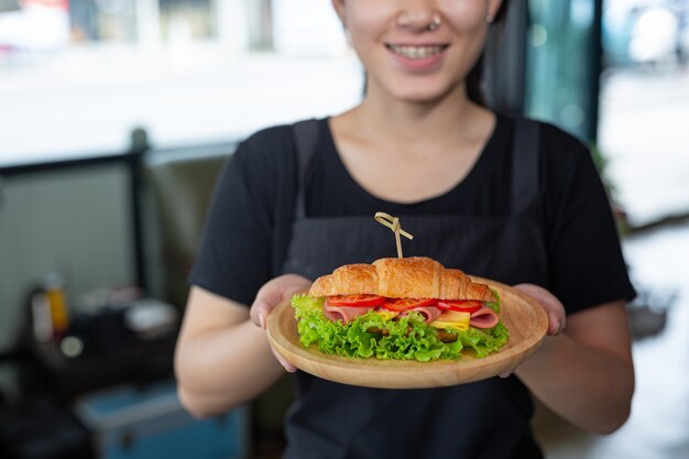 Mujer joven comiendo sándwiches de croissant en la sala de oficina