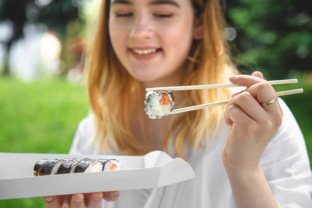 Una mujer joven comiendo sushi en la naturaleza maki roll closeup