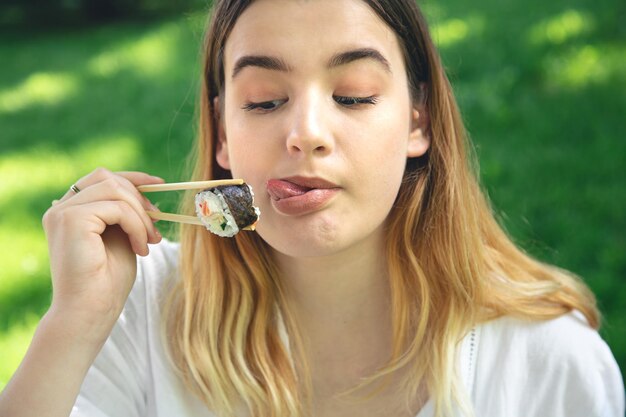 Una mujer joven comiendo sushi en la naturaleza maki roll closeup