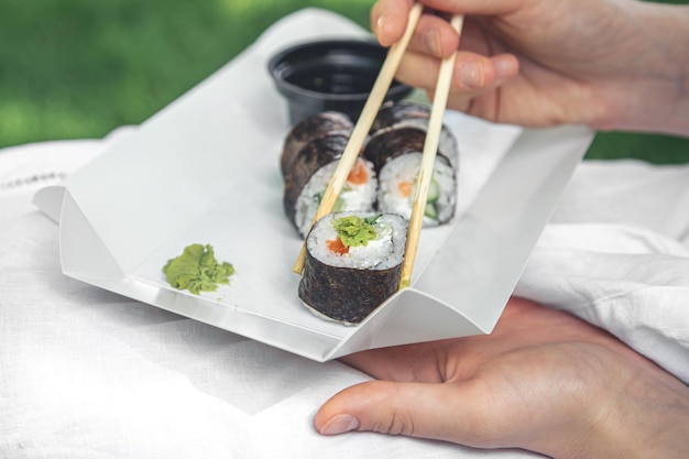 Una mujer joven comiendo sushi en la naturaleza maki roll closeup