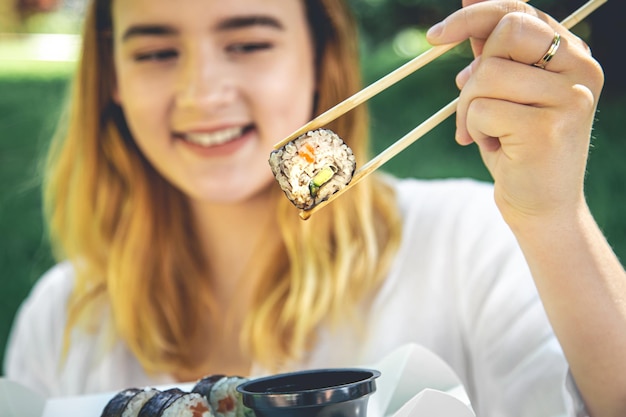 Una mujer joven comiendo sushi en la naturaleza maki roll closeup
