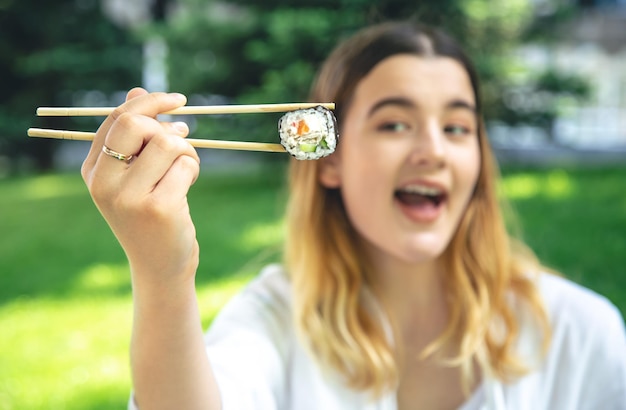 Una mujer joven comiendo sushi en la naturaleza maki roll closeup