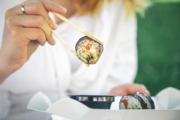 Una mujer joven comiendo sushi en la naturaleza maki roll closeup