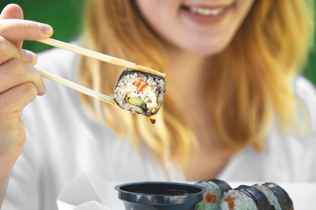 Una mujer joven comiendo sushi en la naturaleza maki roll closeup