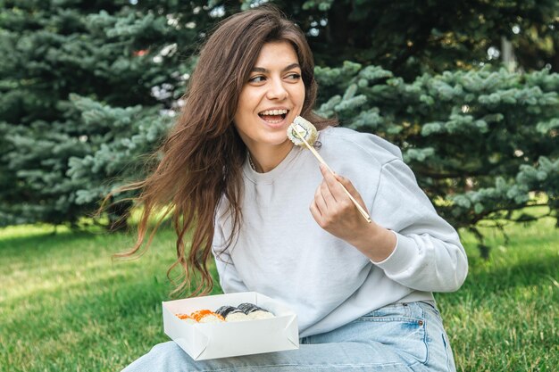 Una mujer joven comiendo sushi en el picnic del parque en la naturaleza