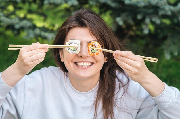 Una mujer joven comiendo sushi en el picnic del parque en la naturaleza