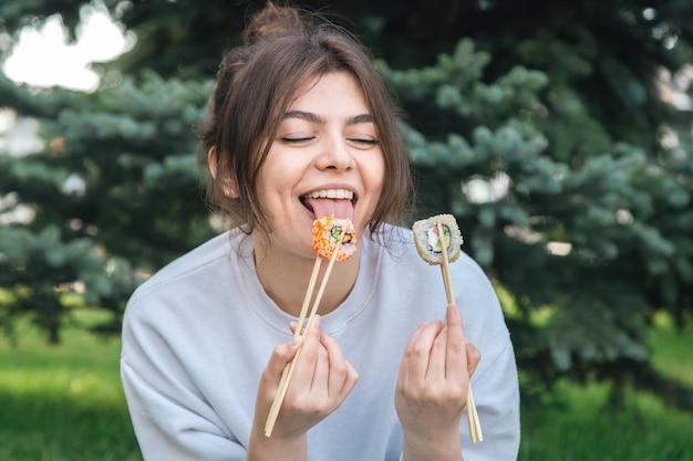 Una mujer joven comiendo sushi en el picnic del parque en la naturaleza