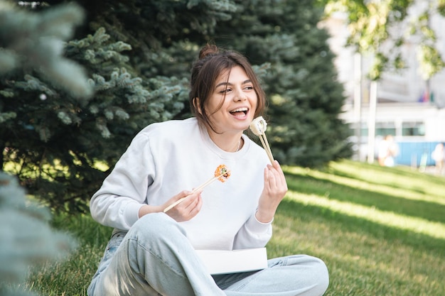 Una mujer joven comiendo sushi en el picnic del parque en la naturaleza