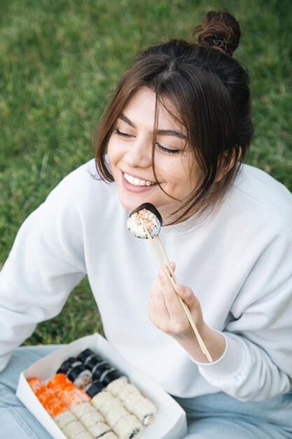 Una mujer joven comiendo sushi en el picnic del parque en la naturaleza