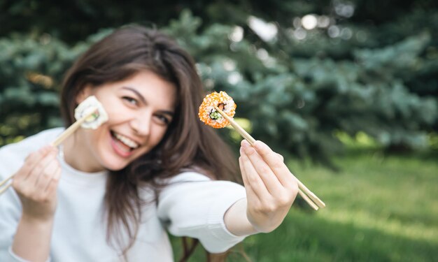 Una mujer joven comiendo sushi en el picnic del parque en la naturaleza
