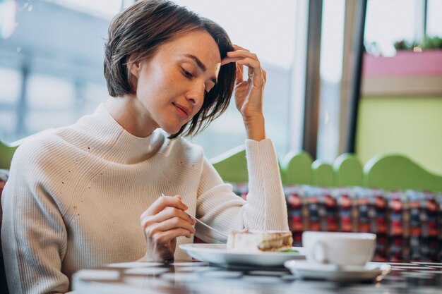 Mujer joven comiendo tiramisú con té en un café