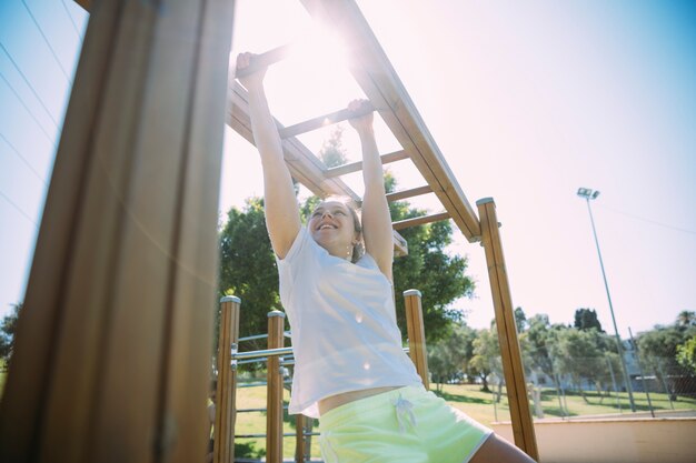 Mujer joven competitiva que ejercita en las barras de mono