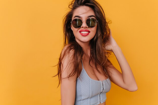 Mujer joven complacida con sonrisa inspirada jugando con cabello oscuro