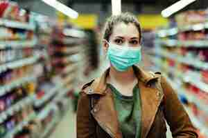 Foto gratuita mujer joven comprando en el supermercado mientras usa una máscara protectora durante la pandemia de virus