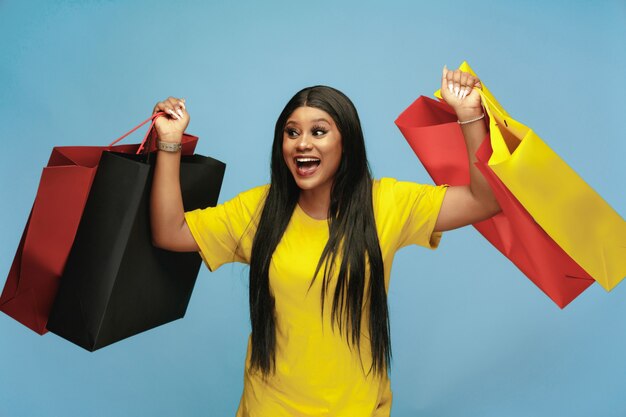 Mujer joven de compras con paquetes de colores en la pared azul