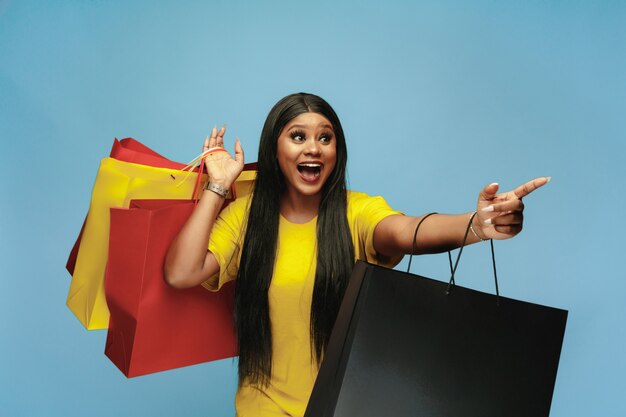Mujer joven de compras con paquetes de colores en la pared azul