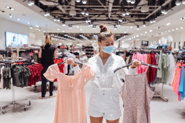 Mujer joven compras ropa en boutique de ropa con mascarilla protectora