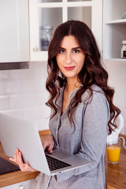 Mujer joven con la computadora portátil en la cocina