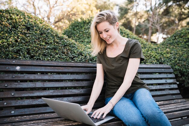 Mujer joven con la computadora portátil en el parque