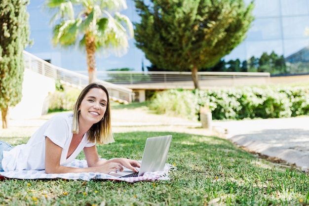 Mujer joven con la computadora portátil que mira la cámara