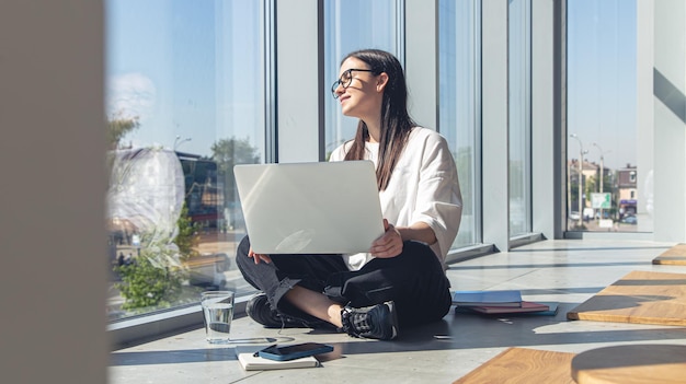 Mujer joven con una computadora portátil en la ventana en una mañana de verano