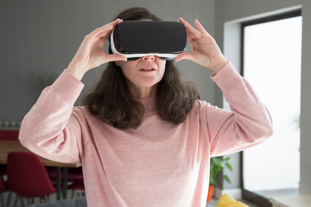 Mujer joven concentrada ajustando gafas de realidad virtual