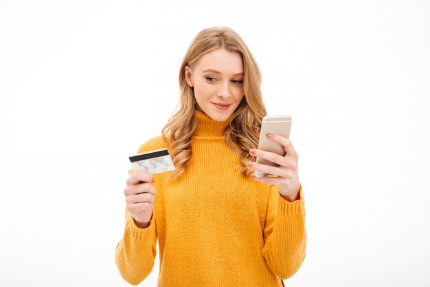 Mujer joven concentrada que sostiene el teléfono móvil y la tarjeta de crédito.