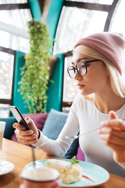 Mujer joven concentrada que usa el teléfono móvil en café.