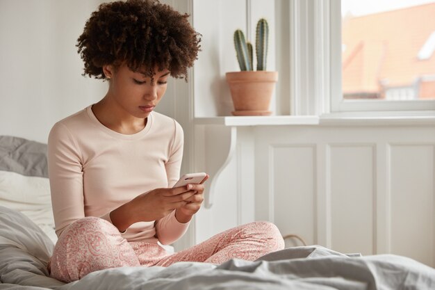 Mujer joven concentrada con su teléfono posando en casa