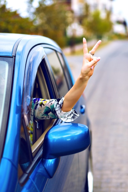 Mujer joven conduciendo un automóvil en el campo, sacó la mano del automóvil y disfrute de su libertad, haciendo una buena ciencia con su mano, concepto de vacaciones de viaje.