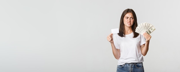 Mujer joven confundida y disgustada mirando dinero y frunciendo el ceño prefiere tarjeta de crédito