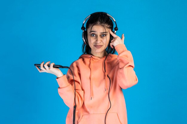 Mujer joven confundida usando auriculares y apuntando su dedo a su cabeza Foto de alta calidad