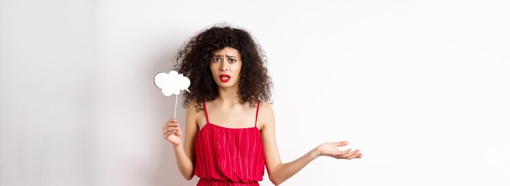 Foto gratuito mujer joven confundida con vestido rojo frunciendo el ceño y mirando molesta sosteniendo un palo de nube de comentarios de pie ag