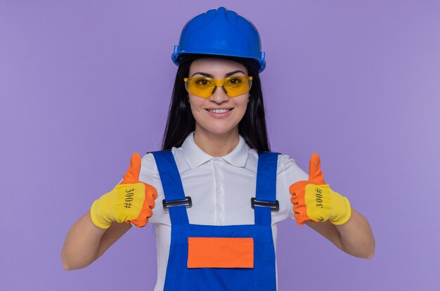 Mujer joven constructor en uniforme de construcción y casco de seguridad con guantes de goma