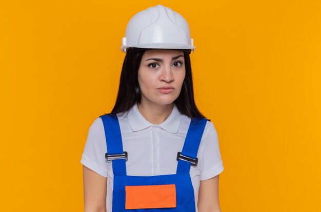 Mujer joven constructor en uniforme de construcción y casco de seguridad mirando a la cámara