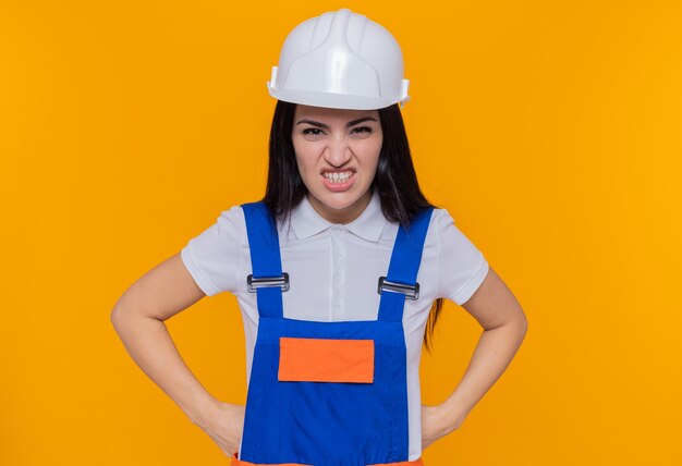 Mujer joven constructor en uniforme de construcción y casco de seguridad mirando a la cámara