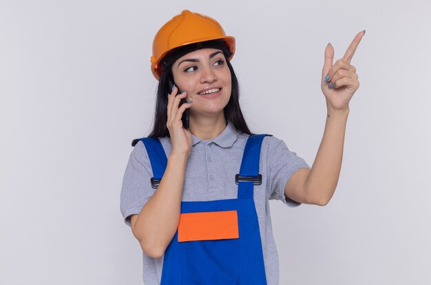 Mujer joven constructor en uniforme de construcción y casco de seguridad mirando a un lado