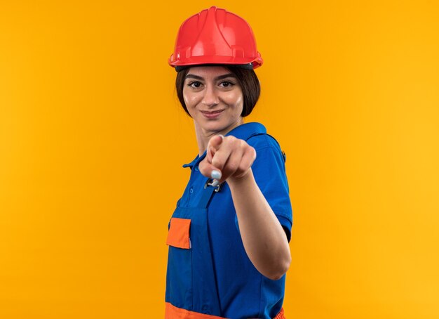 Mujer joven constructora complacida en puntos uniformes aislados en la pared amarilla