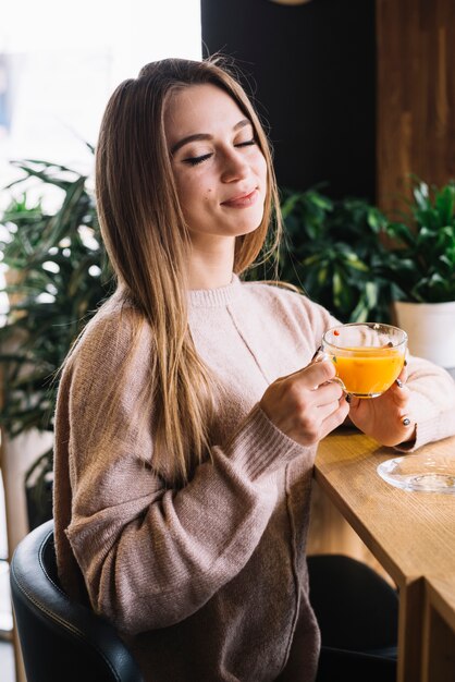 Mujer joven contenta elegante que sostiene la taza de bebida en el contador de la barra en café