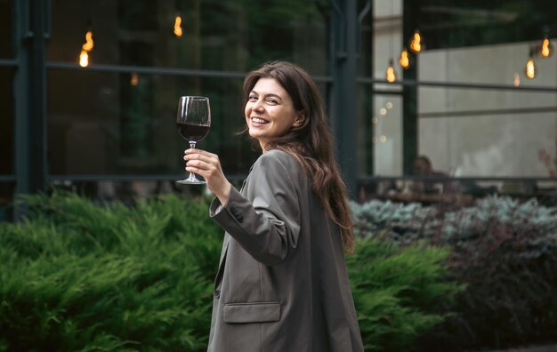 Una mujer joven con una copa de vino afuera cerca de un restaurante