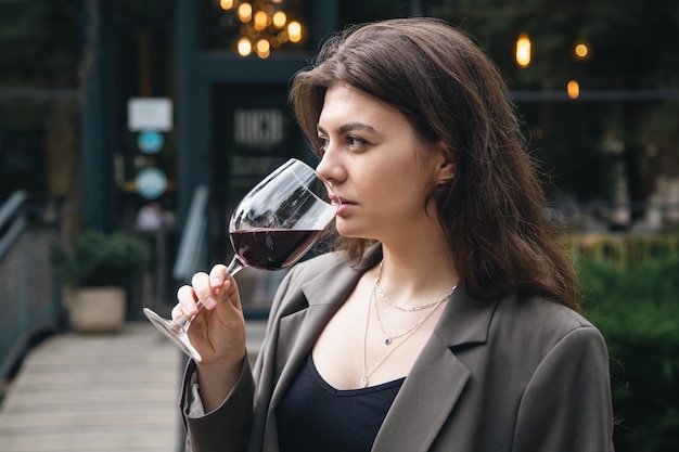 Una mujer joven con una copa de vino afuera cerca de un restaurante